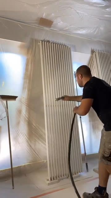 Schilder spuit een designradiator in een volledig afgeschermde ruimte